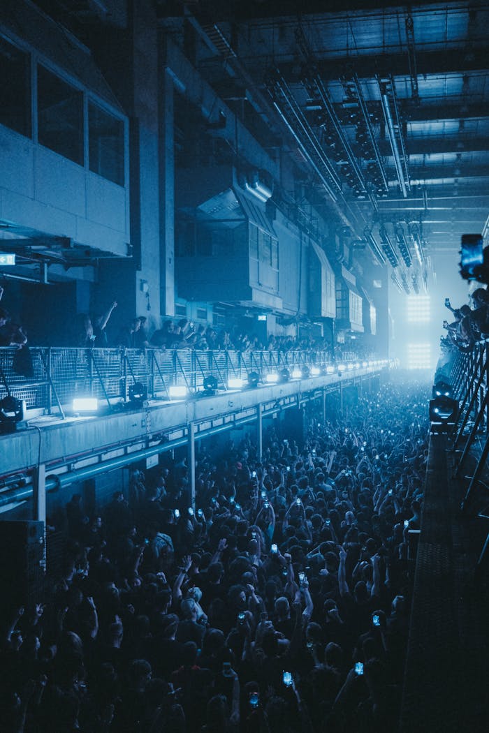 Energetic concert crowd inside industrial venue with dramatic lighting and music vibes.